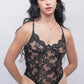 Woman posing in black lace teddy bodysuit with floral lace pattern and scalloped neckline.