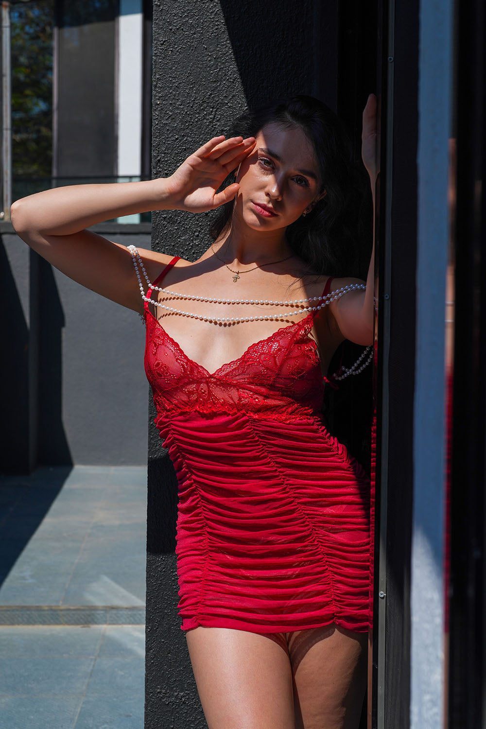 Woman in red lace babydoll with pearl accents posing in sunlight, intimate lingerie for special occasions.