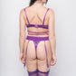 Rear view of a woman wearing a purple satin lingerie set with a thong, garters, and stockings. Ideal for boudoir photoshoots and intimate apparel.