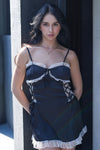 Woman standing outdoors wearing a black satin lace-trim babydoll dress, front view.