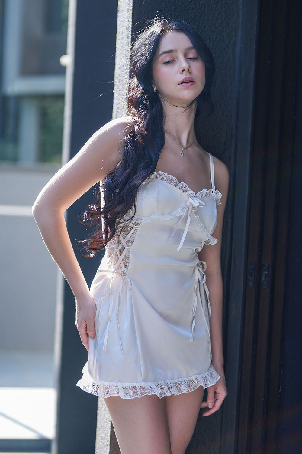 Woman posing outdoors in a white satin lace-trim babydoll dress, front view.