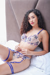 Woman reclining on bed in embroidered lingerie set with blue garters and floral lace detailing.