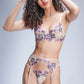 Model wearing nude floral embroidered lingerie set with high-waist garter belt, posing against grey backdrop.